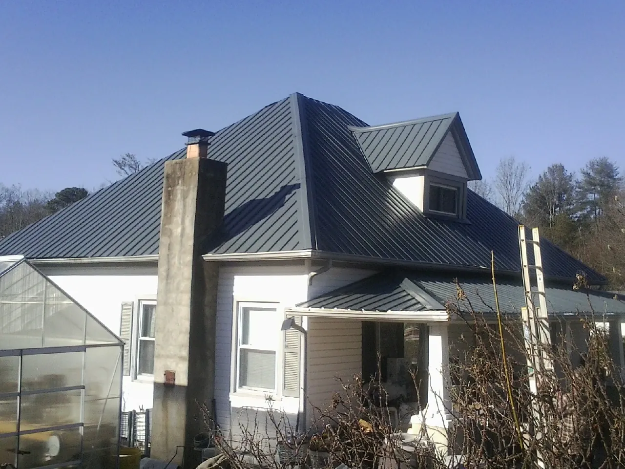 Dark blue standing seam metal roof on a white farmhouse with dormer — Slate & Tile Roof Repair by Roofing Brothers in Montverde