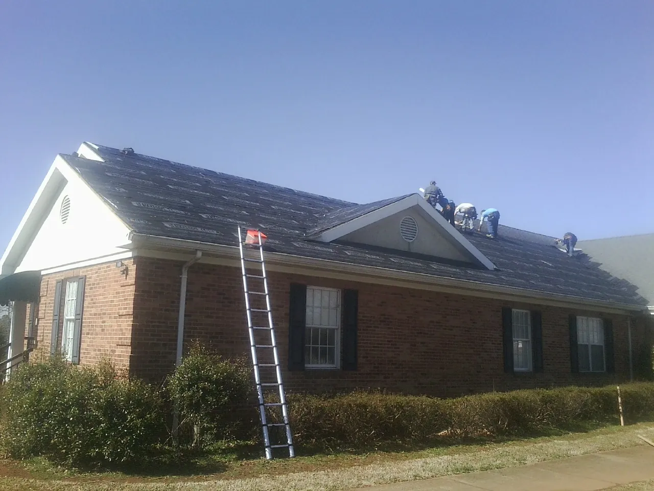 Crew tearing shingles off a brick ranch roof with a ladder set — Emergency Roof Repair work by our crew in Montverde