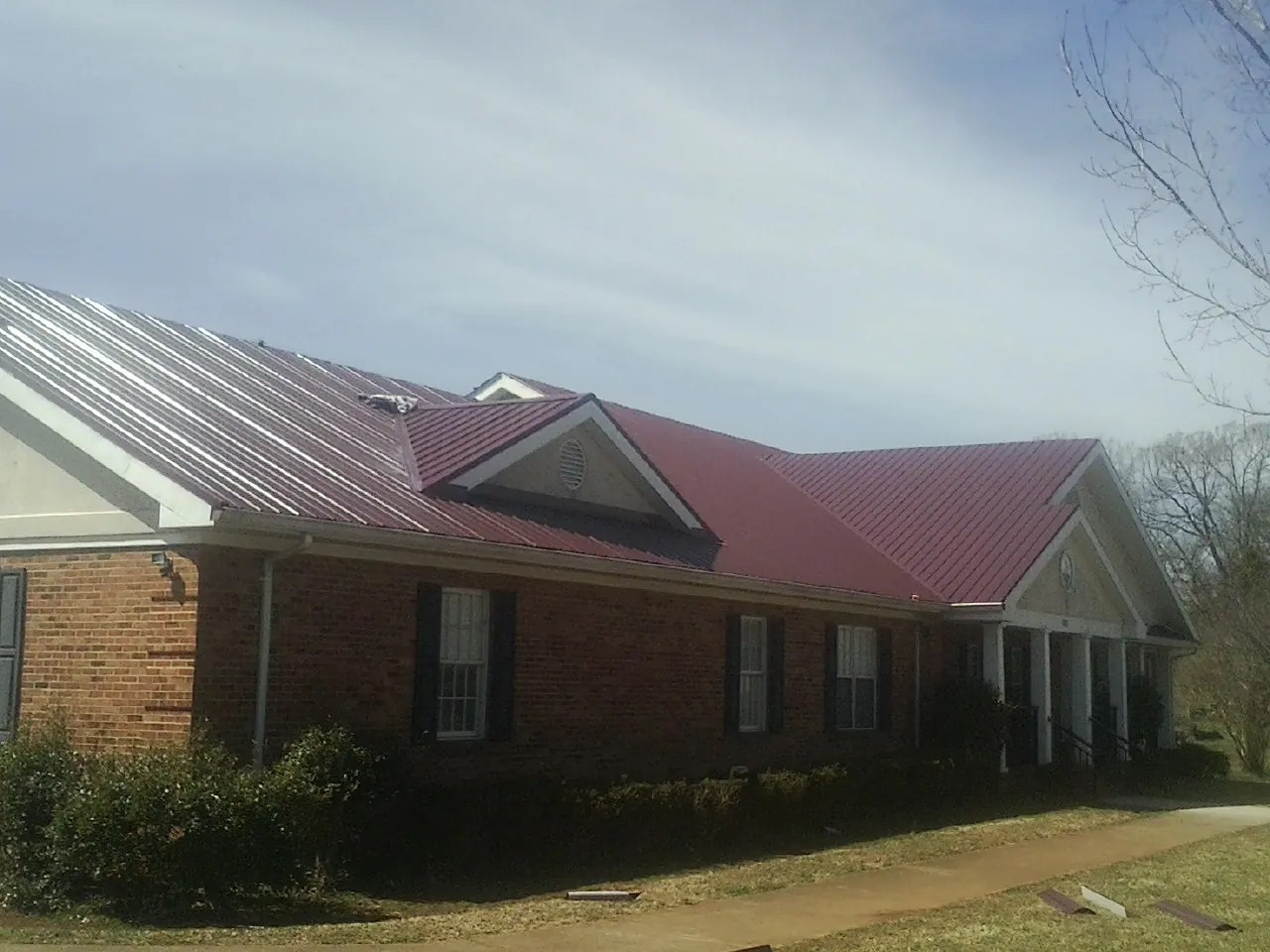 Red metal roof with gabled entries on a long brick building, from a Hail Damage Roof Repair job in Montverde